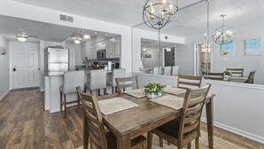 Een moderne keuken met roestvrijstalen apparatuur, een eethoek met houten stoelen en een centrale tafel, en een grote spiegel die de ruimte weerspiegelt.