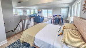A spacious living area with a high ceiling, a dining table, and a view of the ocean through large windows. - Gorgeous New 5 BDR, 4 BA Beach Home With Tower Outlook Suite! (Cape Charles)