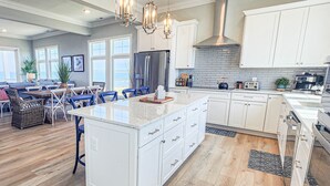 A spacious kitchen with white cabinetry, a large island, and a central island with a built-in stove. There are pendant lights above the island and a stainless steel range hood above the stove. - Gorgeous New 5 BDR, 4 BA Beach Home With Tower Outlook Suite! (Cape Charles)