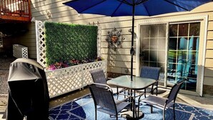 Eine Terrasse im Freien mit Tisch und Stühlen, einem Grill und einem weißen Spalierzaun sowie einer grünen Wand.