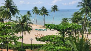 Ein Strand mit Palmen, einem Schild mit der Aufschrift "PHUQUOC" und einem sandigen Bereich mit Außenbestuhlung.