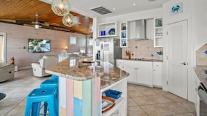 Una cucina moderna con mobili bianchi, un'isola con piano in granito e una zona pranzo con divano bianco e sgabelli blu.