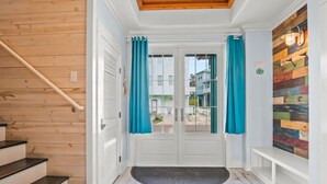 Un corridoio con una scala in legno, una porta bianca con tende color acquamarina e un muro di legno colorato.