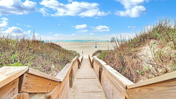 Una passerella in legno che conduce a una spiaggia, con dune da entrambi i lati.