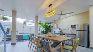 A modern kitchen with a dining area, featuring a wooden table and chairs, a stainless steel refrigerator, and hanging plants.