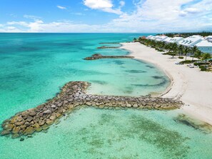 Une station balnéaire dotée d’eaux turquoise et limpides, d’une plage de sable fin et d’une rangée de bâtiments blancs aux toits rouges.