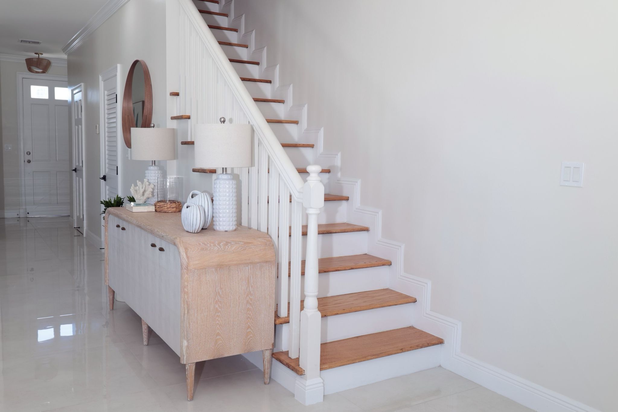 Una escalera con barandillas blancas y peldaños de madera, que lleva a una plataforma con una consola blanca y un espejo.