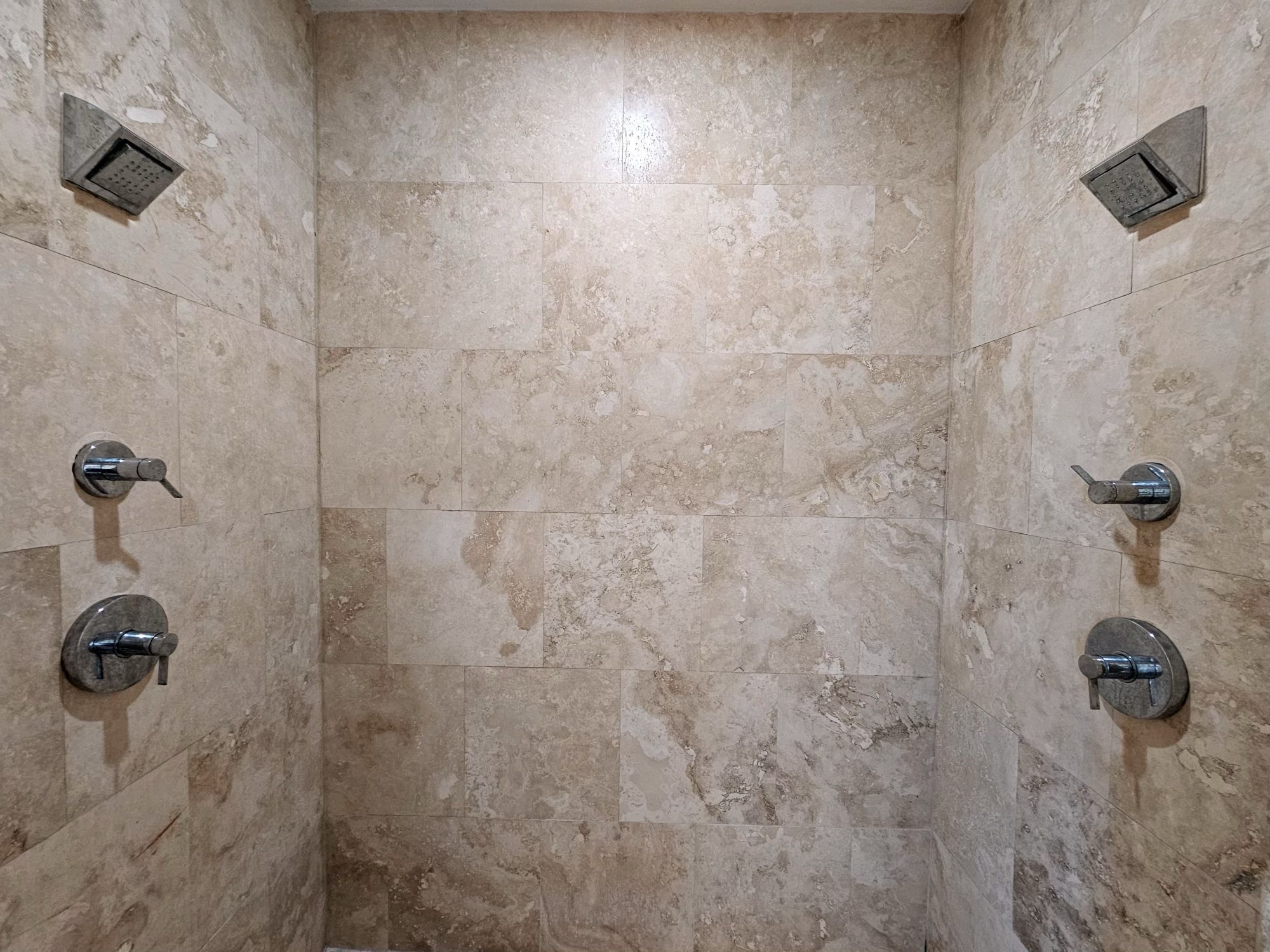 A tiled shower enclosure with a rectangular layout, a central drain, and two wall-mounted faucets.