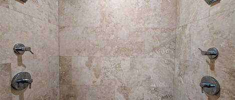 A tiled shower enclosure with a rectangular layout, a central drain, and two wall-mounted faucets.