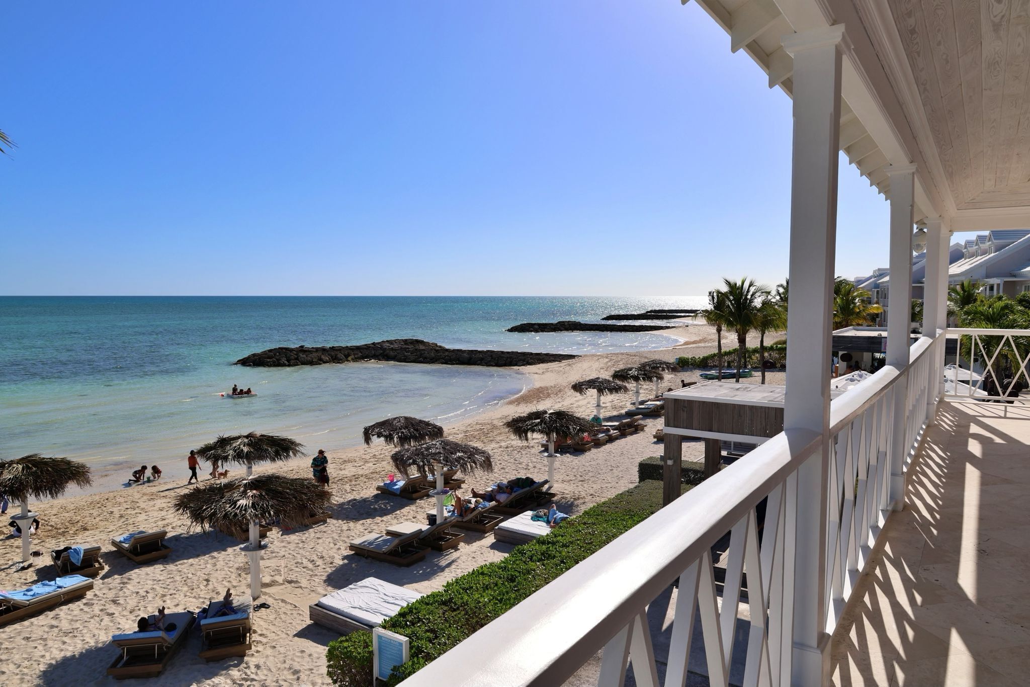 Blick auf einen Strand mit Liegestühlen und Sonnenschirmen, einem klaren Himmel und ruhiger See.