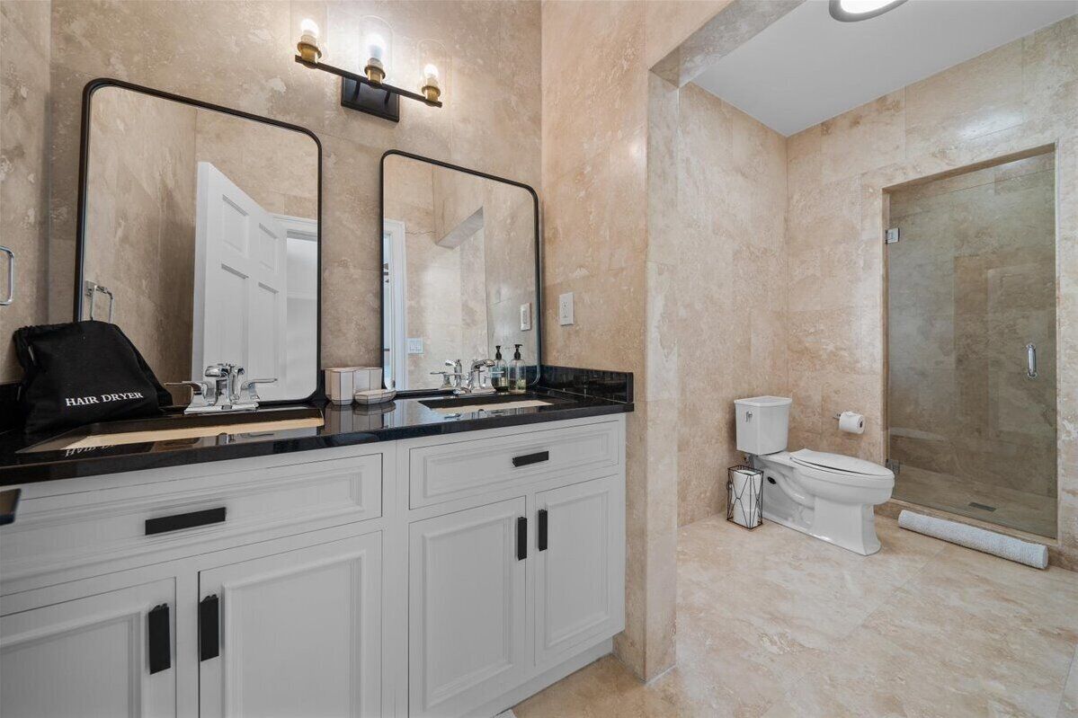 A bathroom with a large mirror, a sink, a toilet, and a shower area.