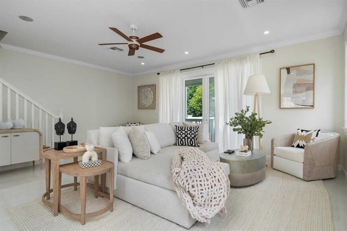 A modern living room with a sofa, coffee table, and armchair, a ceiling fan, and a staircase with white railings.