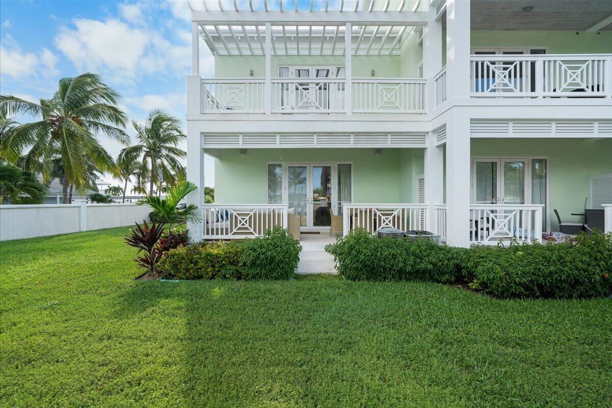 A two-story building with a light green facade, white balconies, and a well-maintained lawn with palm trees.