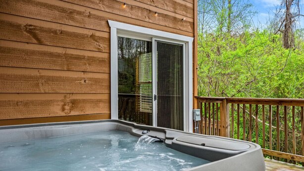 A hot tub on a wooden deck with a sliding glass door leading to a covered patio.