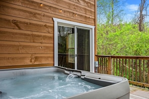 Un jacuzzi en una terraza de madera con una puerta corrediza que da a un porche cubierto.