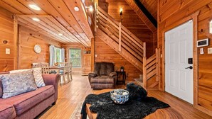 A cozy log cabin interior with a living room, dining area, and a staircase leading to an upper level.