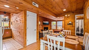 A wooden cabin interior with a dining area, kitchen, and living room.
