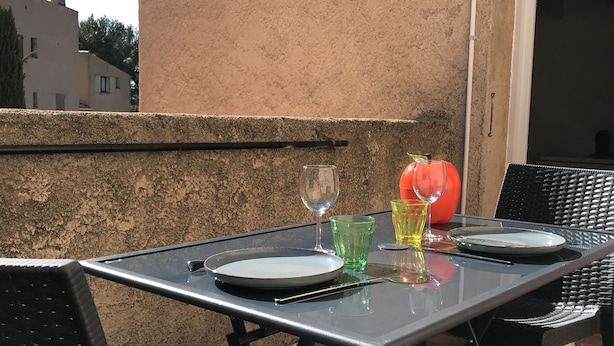 An outdoor patio with a table set for two, featuring a glass top and metal chairs.