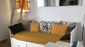 A compact living space with a sofa bed, a small table, a ladder, and a microwave.