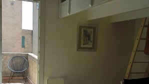 A room with a balcony, a white chair, a bed, and a ladder.
