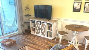 A cozy living room with a wicker sofa, a wooden coffee table, a TV on a white cabinet, and a small round table with chairs. - Oceanfront ! All linens included ! Stunning view ! 2BR/2BA.  WindJammer Condos (Ocean Isle Beach)