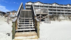 A wooden staircase leading to a building with multiple balconies, situated on a sandy beach. - Oceanfront ! All linens included ! Stunning view ! 2BR/2BA.  WindJammer Condos (Ocean Isle Beach)
