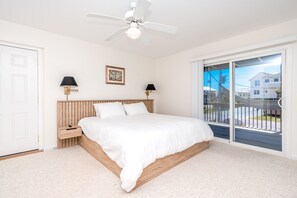 A bedroom with a bed, a ceiling fan, a nightstand, two wall lamps, a framed picture, and a view through a sliding glass door.