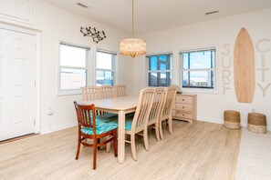 A dining area with a wooden table and chairs, a chandelier, and a surfboard decoration on the wall.