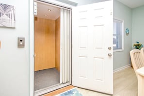 A room with a white door, a wooden floor, a light-colored wall, and a window with blinds.