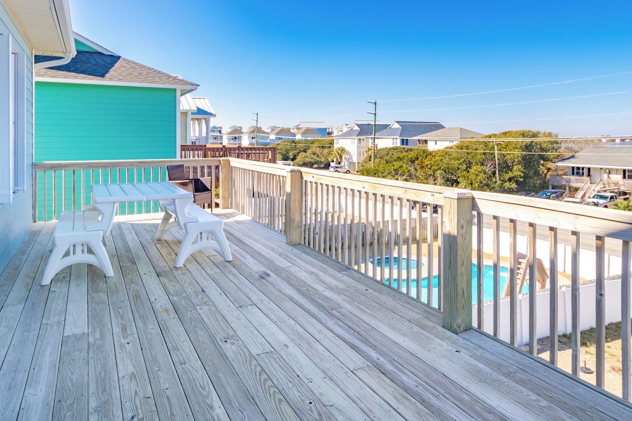 A wooden deck with a pool, white chairs, and a view of houses in the background.