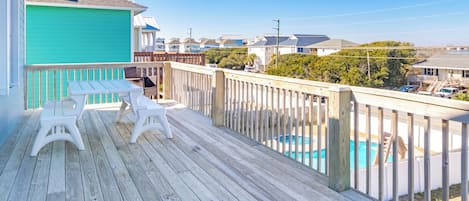 A wooden deck with a pool, white chairs, and a view of houses in the background.
