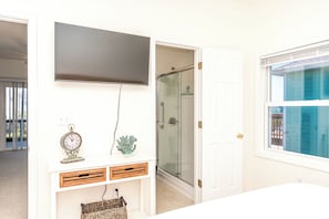 A bathroom with a glass shower enclosure, a mounted television, and a visible door leading to another room.