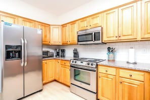 A kitchen with wooden cabinets, a stainless steel refrigerator, a microwave, a stove, and a coffee maker. - The Salty Beagle - 4BR Home with Pool; Ocean & Sound Views (Surf City)