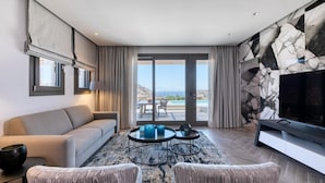 A modern living room with a sofa, two armchairs, a coffee table, and a TV. The room has a large window with a view of the outdoors. - Remarkable 7-bed Villa in Mikonos - Villa Ataraxia (Mykonos)