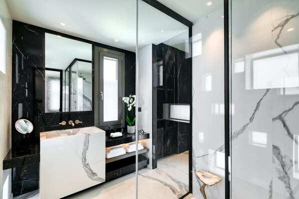 A modern bathroom with a black and white marble vanity, a large mirror, and a glass shower enclosure.