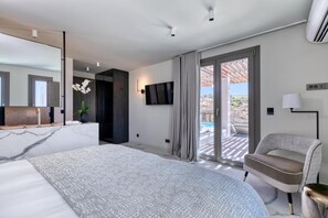 A modern hotel room with a large bed, a seating area, a TV, and a view of the outdoors.