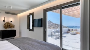 A modern bedroom with a large bed, a TV mounted on the wall, and a balcony with a view of the sea. - Remarkable 7-bed Villa in Mikonos - Villa Ataraxia (Mykonos)