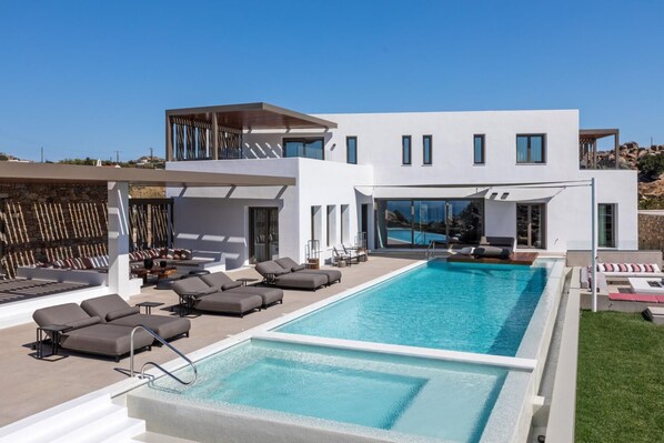 A modern house with a large swimming pool, outdoor seating, and a view of the surrounding landscape.