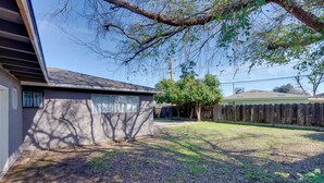 A residential backyard with a house, a wooden fence, and a tree. - Near Airport & Dtwn: Breezy Fresno Home! (Fresno)