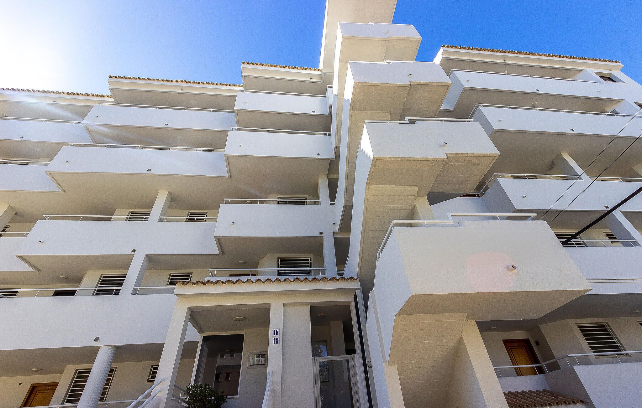 Un edificio residencial de varios pisos con balcones, techo de tejas y cielo despejado.