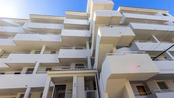 Un edificio residencial de varios pisos con balcones, techo de tejas y cielo despejado.