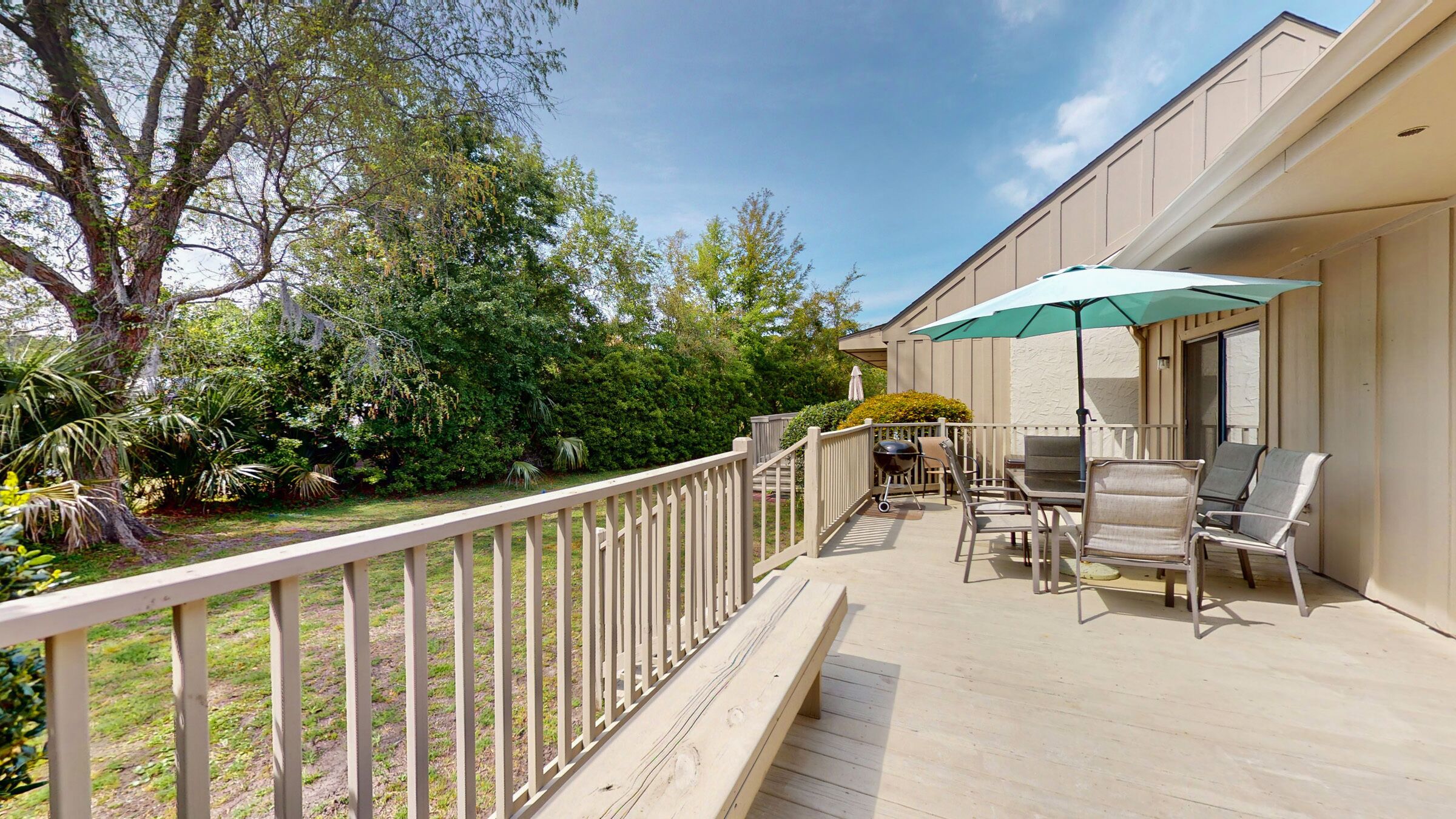 Eine Terrasse mit Gartenmöbeln, einem Grill und einem großen Sonnenschirm.