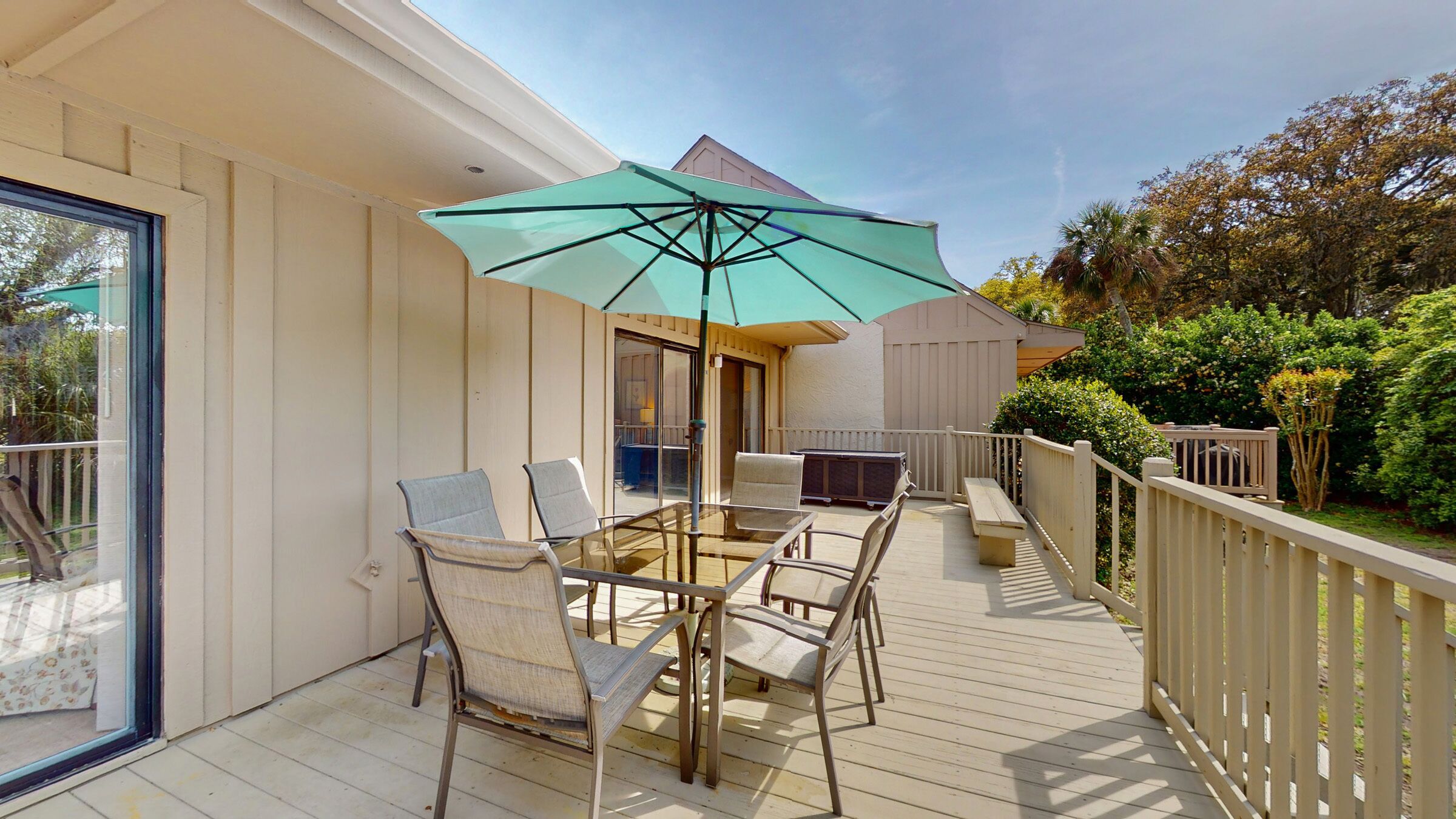 A deck with a glass table and chairs, an umbrella, and a view of the backyard.