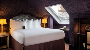 Habitació d'hotel amb un llit gran, dues làmpades laterals, una taula petita amb làmpada i un finestral.
