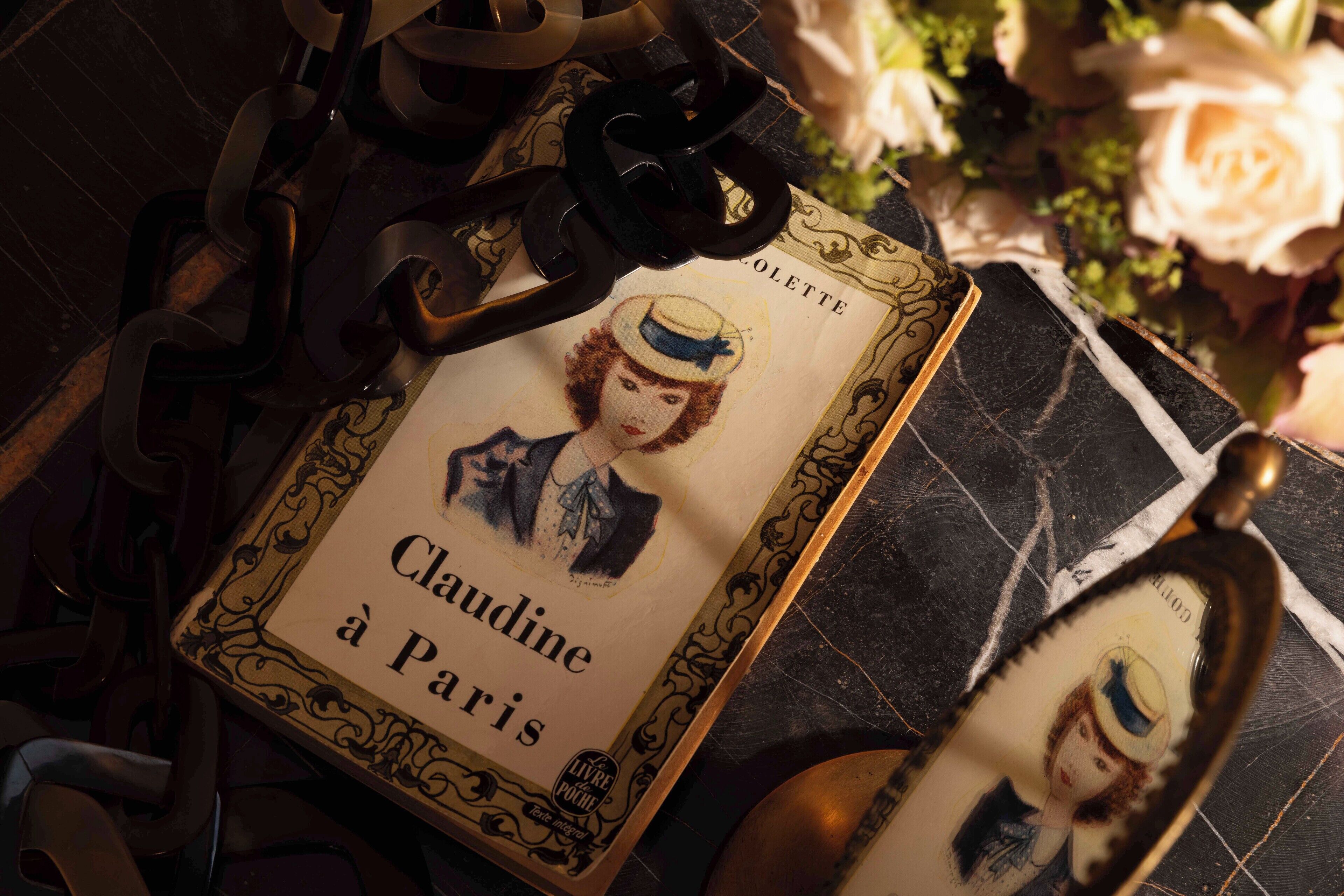 A vintage book titled 'Claudine à Paris' with ornate, gold-trimmed edges, placed on a dark, textured surface.