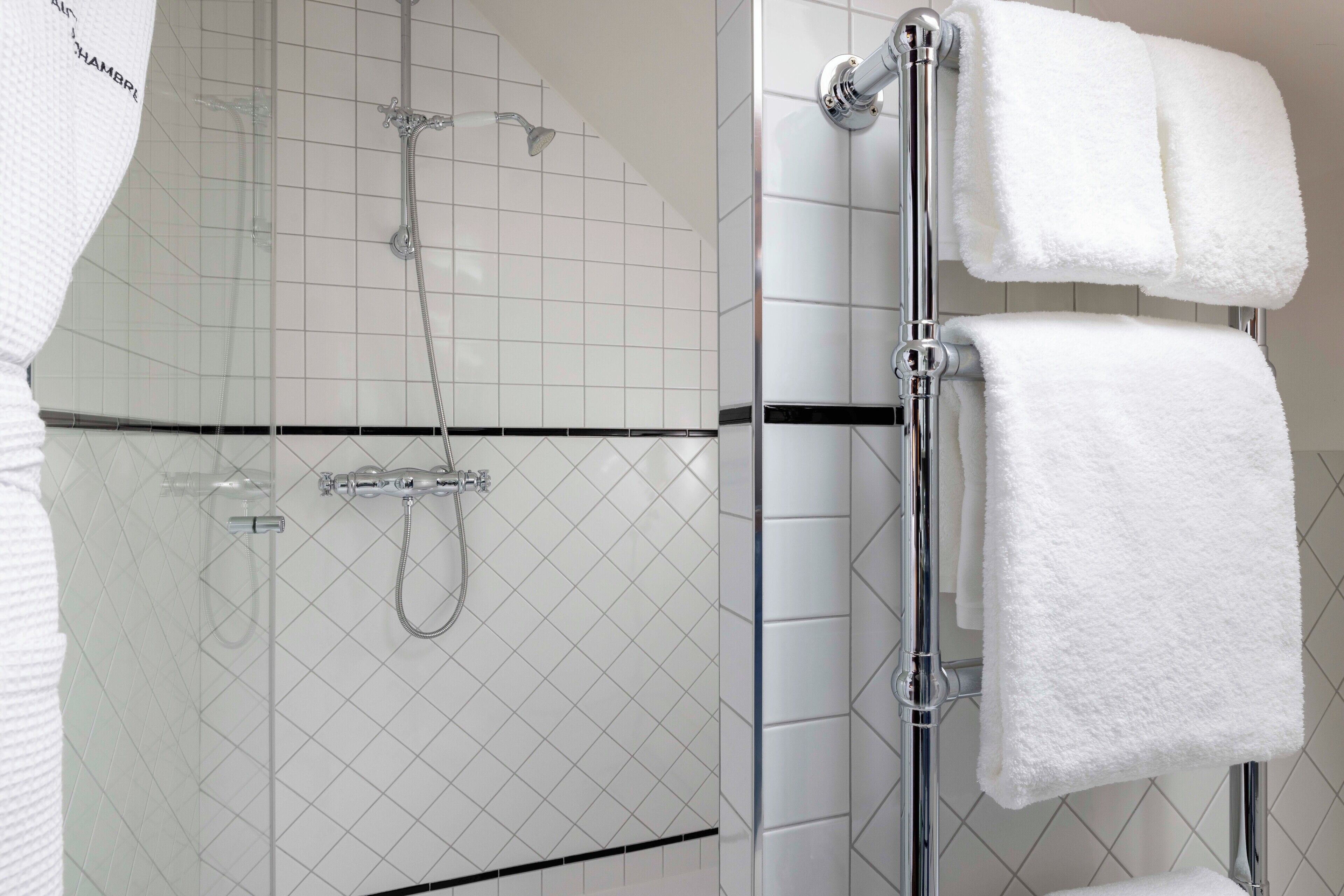 Une salle de bain avec une douche à parois de verre, des robinetteries chromées et des serviettes blanches rangées sur un porte-serviettes.
