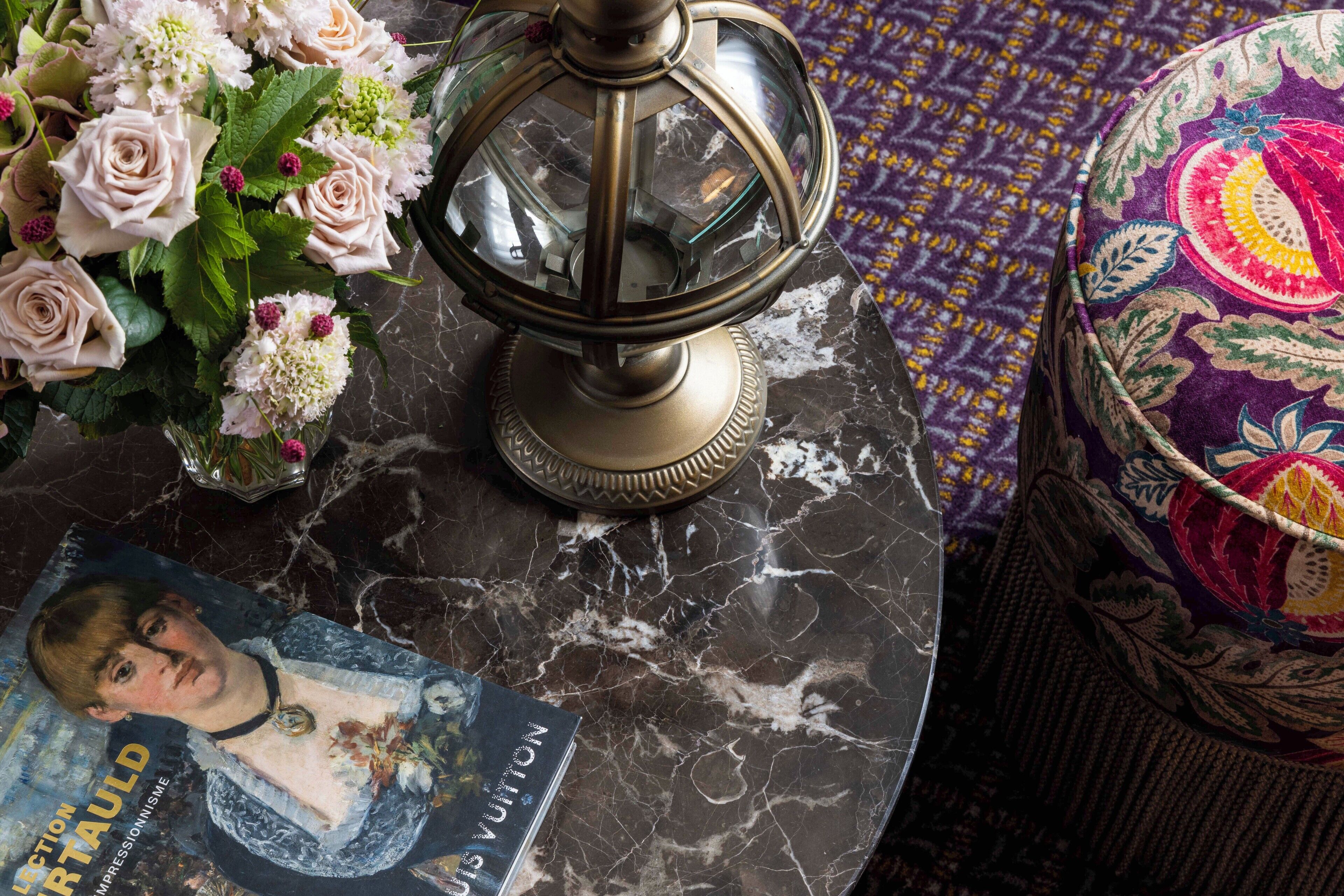 A marble table with a vintage-style lamp, a floral arrangement, and a magazine.