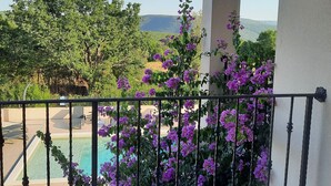 Un balcone con vista su una piscina, circondato da fiori viola e vegetazione.