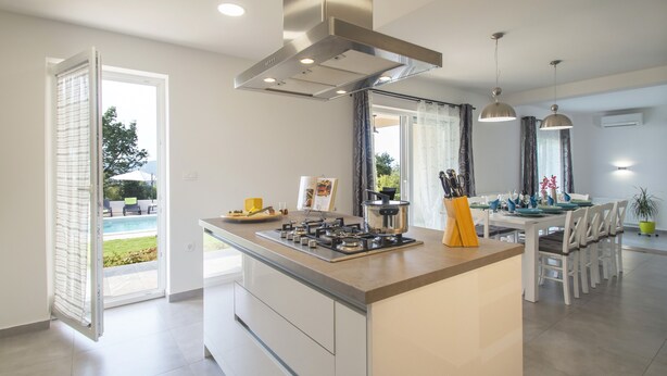 Una cucina moderna con isola centrale, zona pranzo con tavolo e sedie, e vista su una piscina.
