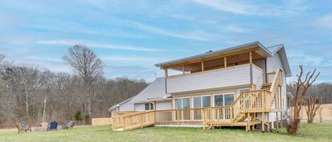 A two-story house with a wooden deck, a covered porch, and a large window overlooking a grassy yard.